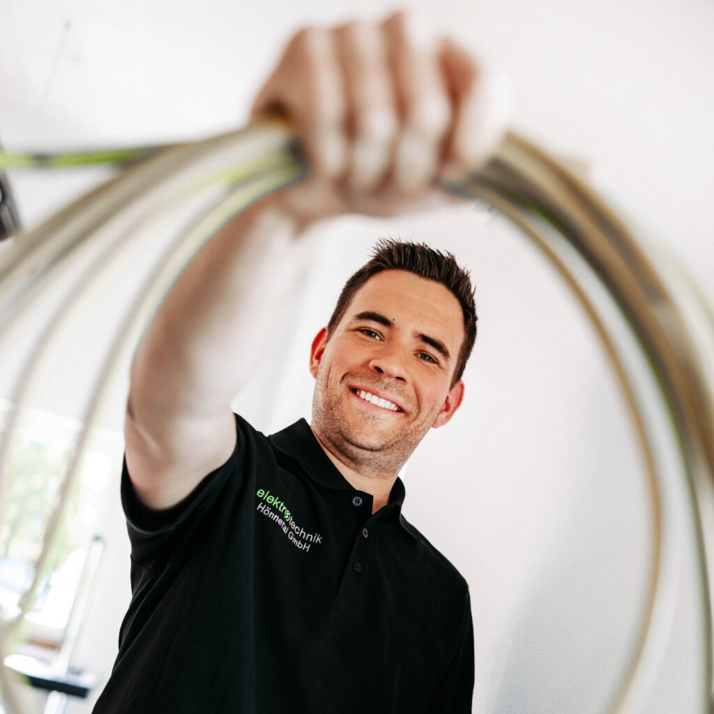Ein Elektriker der Elektrotechnik Hönnetal hält ein Kabel für die Elektroinstallation in die Kamera.