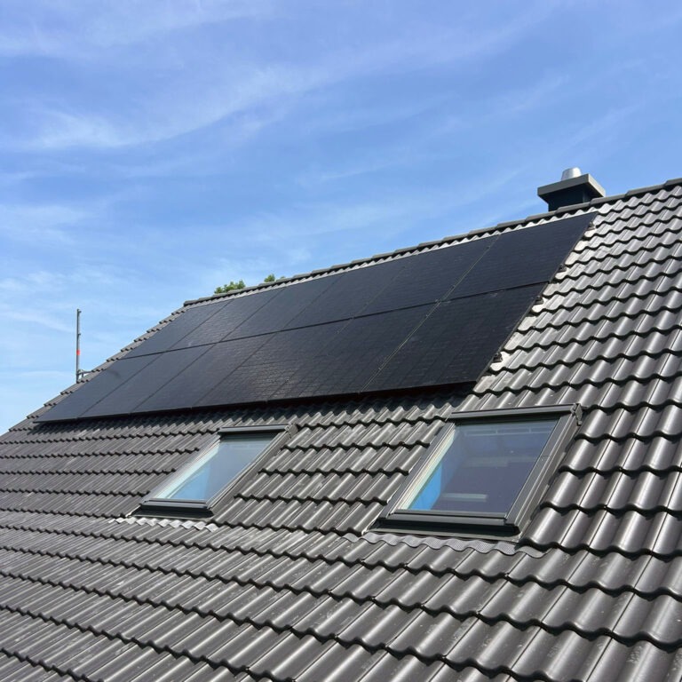 Ein großes Dach mit dunklen Ziegeln wurde von der Elektrotechnik Hönnetal in der linken oberen Hälfte mit Solarpaneelen einer Photovoltaik-Anlage bedeckt.