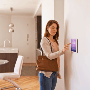 Eine Frau steht in ihrem Esszimmer und bedient ein Tablet an der Wand, auf dem ein Smart Home System installiert ist.